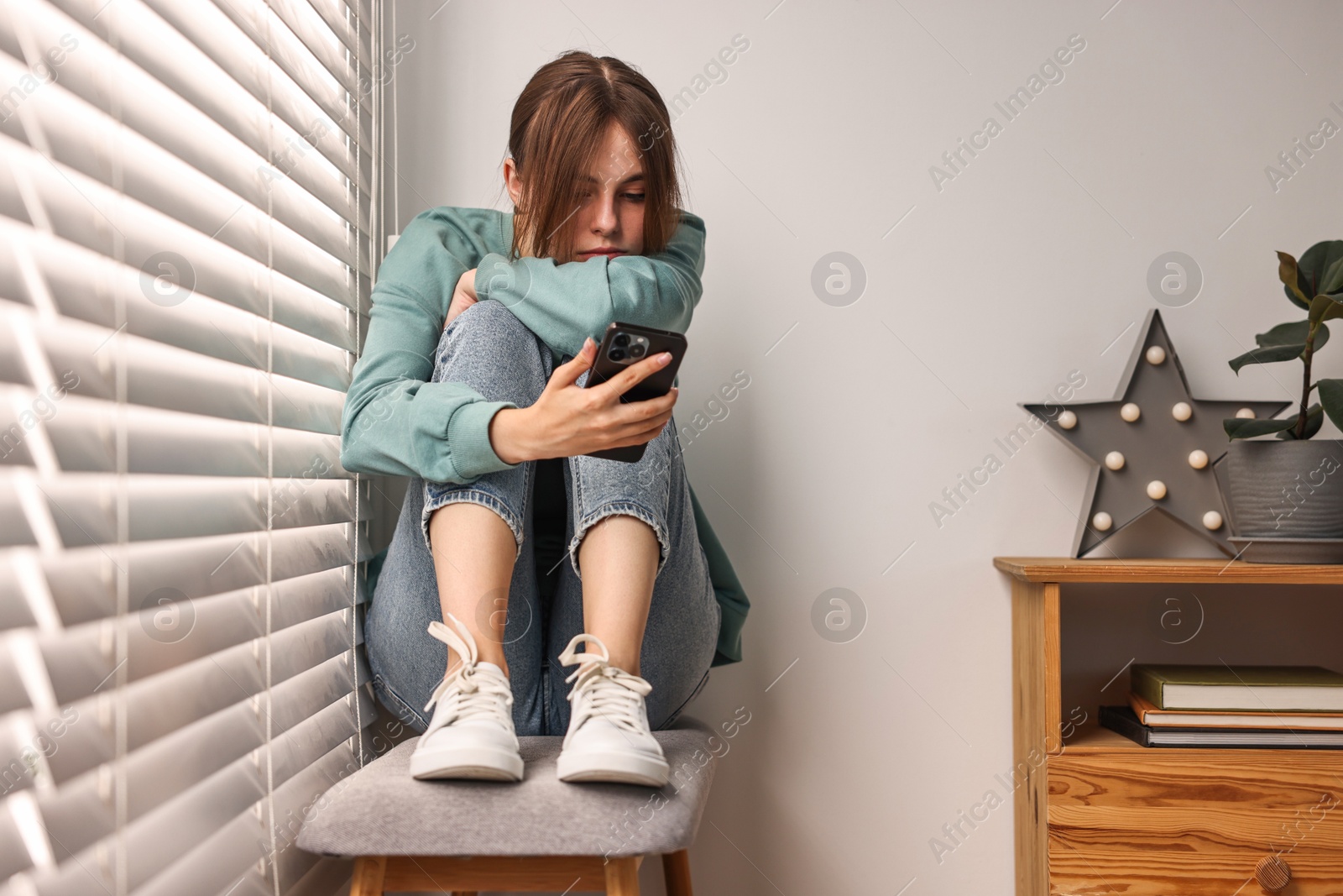 Photo of Loneliness concept. Sad teenage girl using smartphone at home