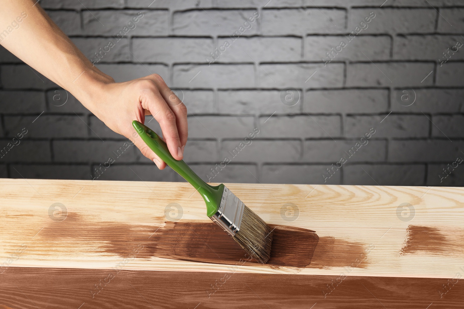 Photo of Woman with brush applying walnut wood stain onto wooden surface, closeup