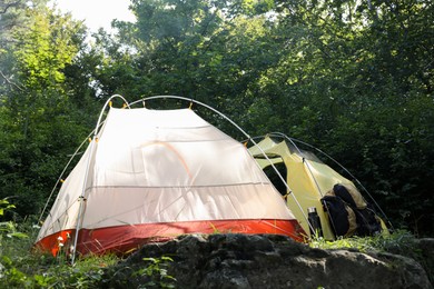 Modern camping tents, backpack and bottle in forest