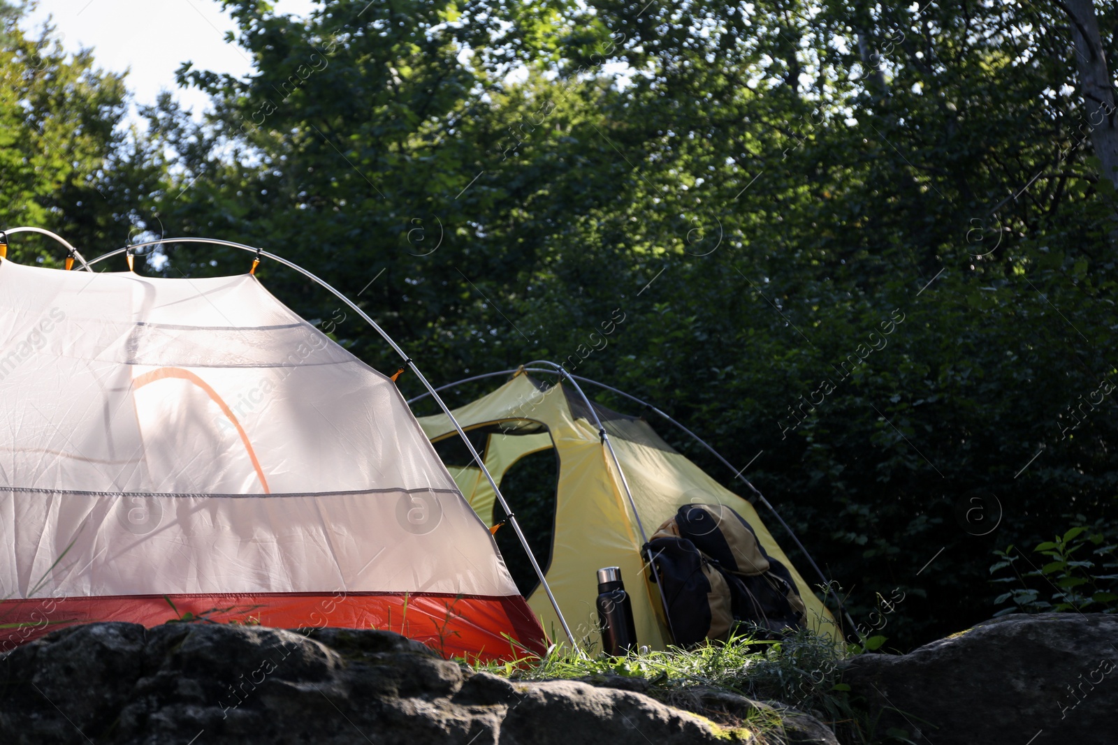 Photo of Modern camping tents, backpack and bottle in forest