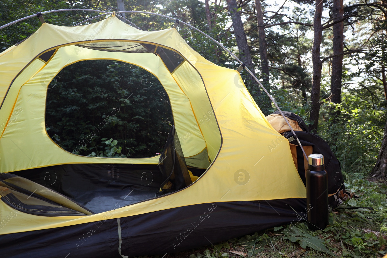 Photo of Modern camping tent, backpack and bottle in forest