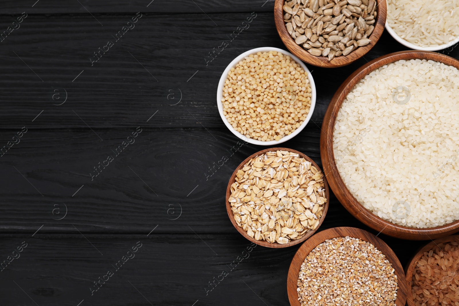 Photo of Different types of cereals and seeds in bowls on black wooden table, flat lay. Space for text