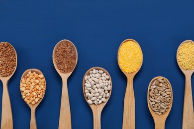 Different types of cereals, seeds and legumes in spoons on blue wooden table, flat lay