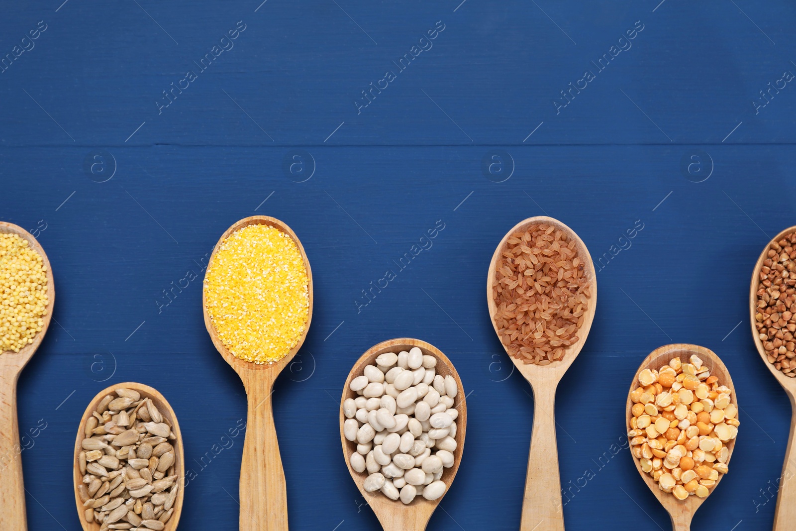 Photo of Different types of cereals, seeds and legumes in spoons on blue wooden table, flat lay. Space for text