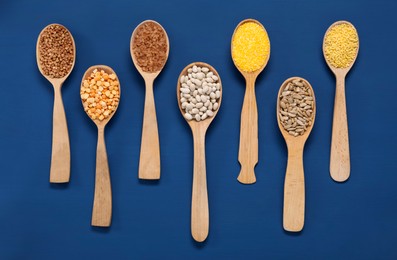 Photo of Different types of cereals, seeds and legumes in spoons on blue wooden table, flat lay