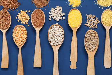 Photo of Different types of cereals, seeds and legumes in spoons on blue wooden table, flat lay