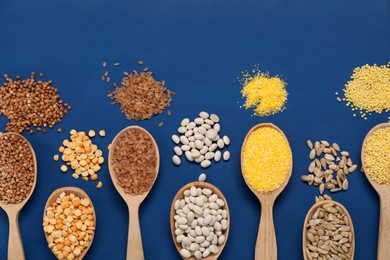 Different types of cereals, seeds and legumes in spoons on blue wooden table, flat lay