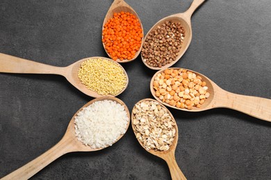 Photo of Different types of cereals and legumes in wooden spoons on grey table, flat lay