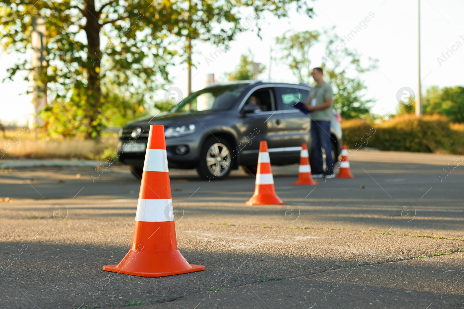 Photo of Examiner instructing student before exam at driving school test track, focus on traffic cone