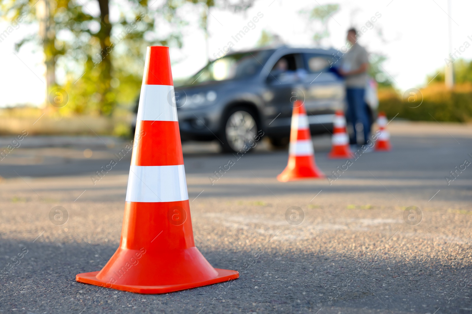 Photo of Examiner instructing student before exam at driving school test track, focus on traffic cone