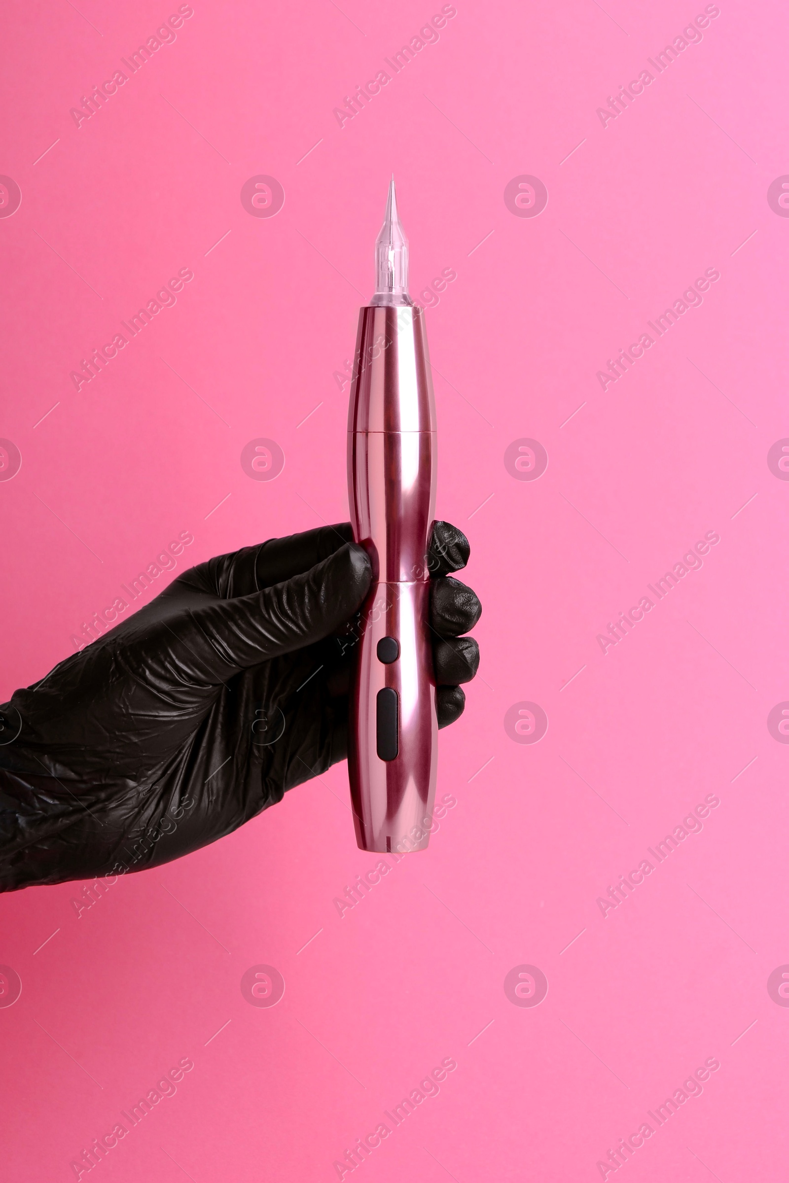 Photo of Professional cosmetologist holding permanent makeup machine on pink background, closeup