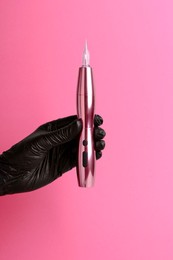 Photo of Professional cosmetologist holding permanent makeup machine on pink background, closeup