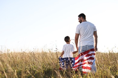 Photo of Father and son with flag of USA outdoors, back view. Space for text