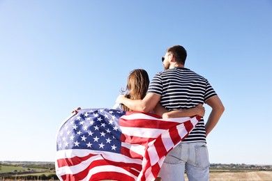 Photo of Couple with flag of USA outdoors, back view