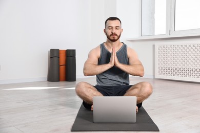 Photo of Man meditating near laptop on yoga mat at home. Space for text