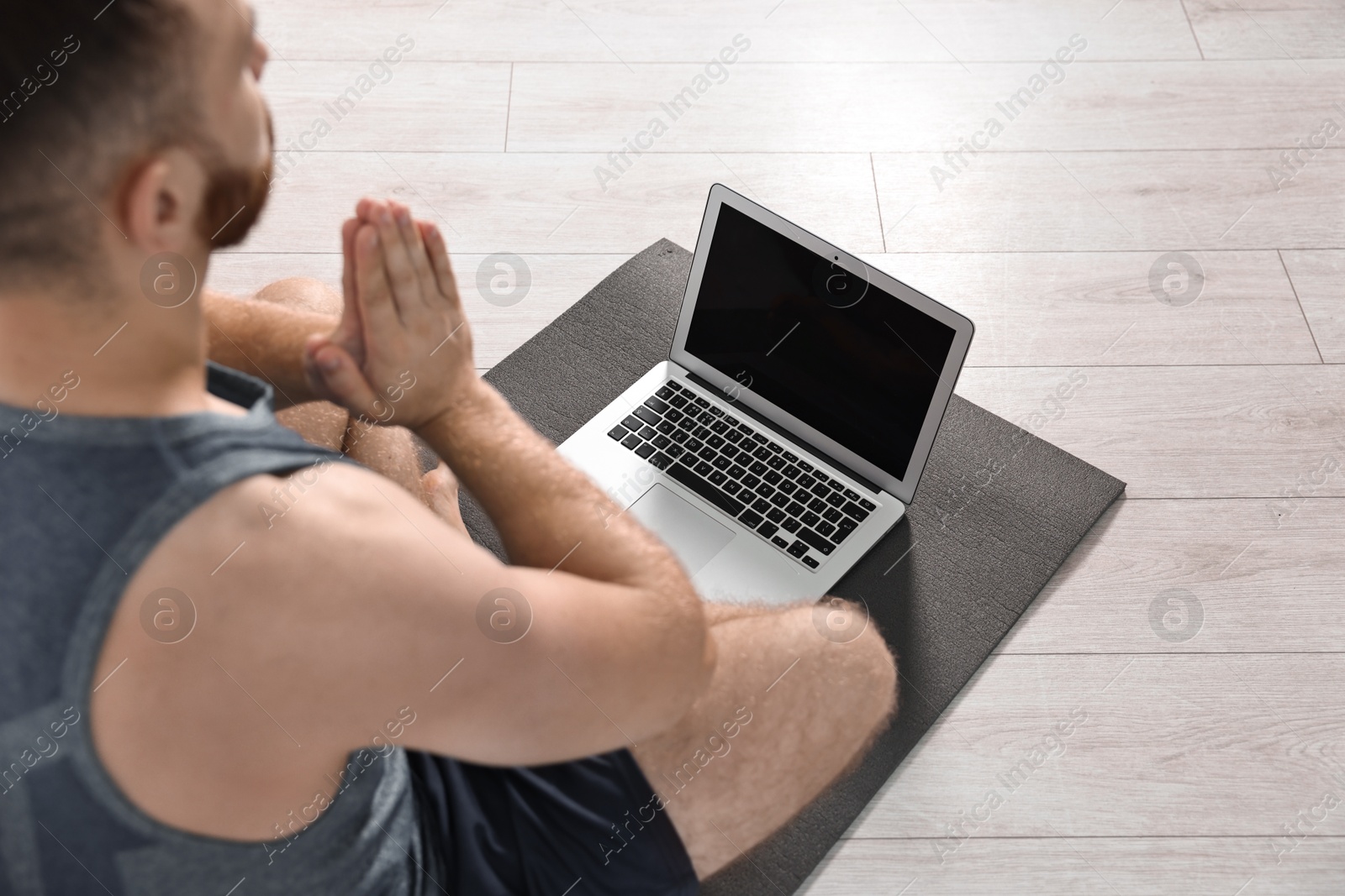 Photo of Man meditating near laptop on yoga mat at home, closeup