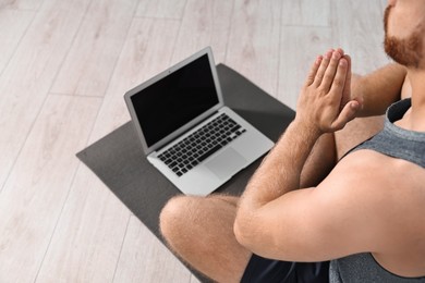 Photo of Man meditating near laptop on yoga mat at home, closeup