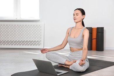 Woman meditating near laptop on yoga mat at home. Space for text