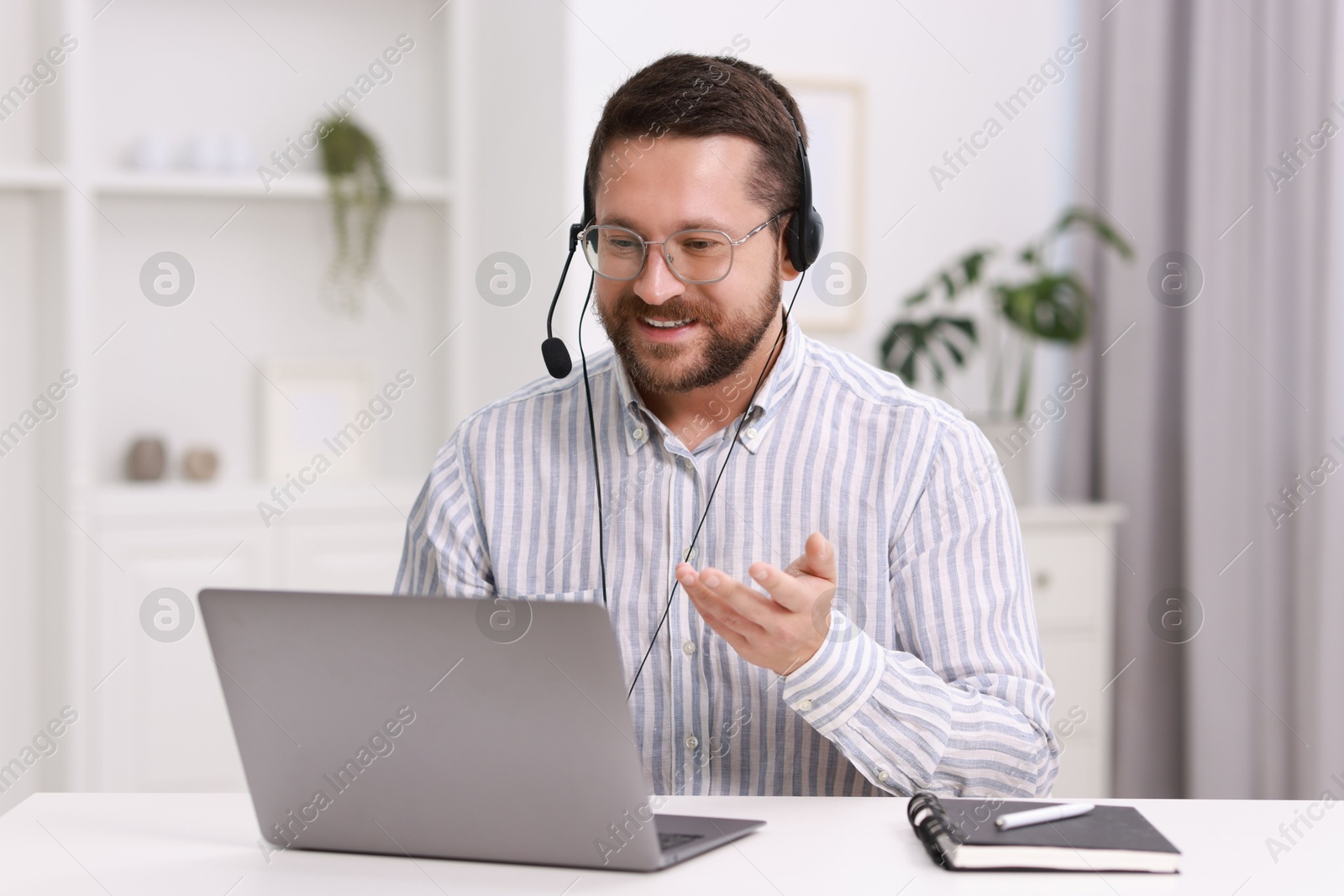 Photo of Interpreter in headset having video chat via laptop at white table indoors