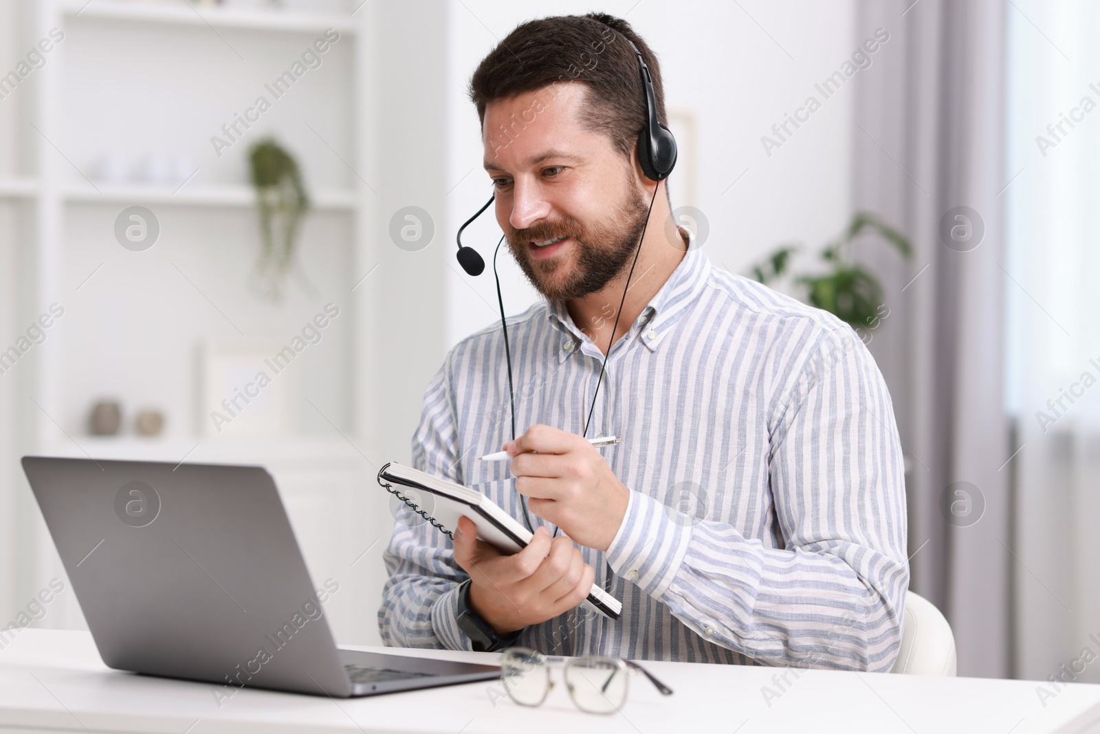 Photo of Interpreter in headset having video chat via laptop at white table indoors