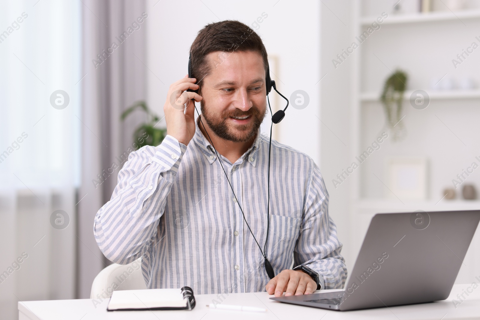 Photo of Interpreter in headset having video chat via laptop at white table indoors