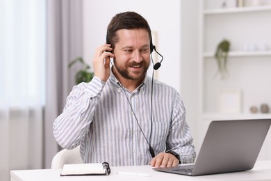 Photo of Interpreter in headset having video chat via laptop at white table indoors