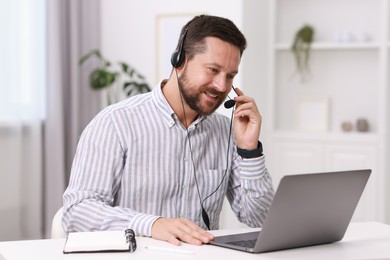 Photo of Interpreter in headset having video chat via laptop at white table indoors