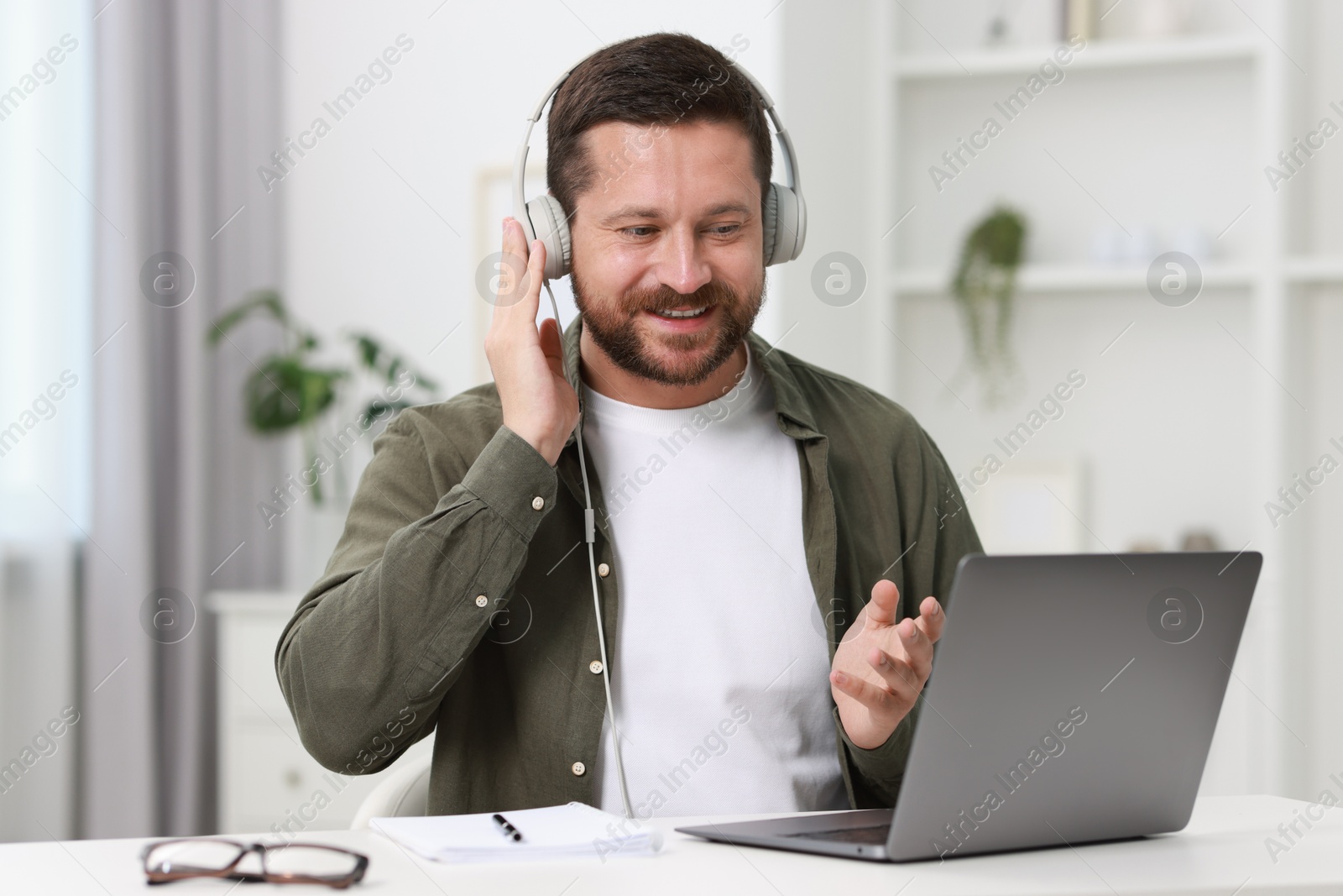 Photo of Interpreter in headphones having video chat via laptop at white table indoors