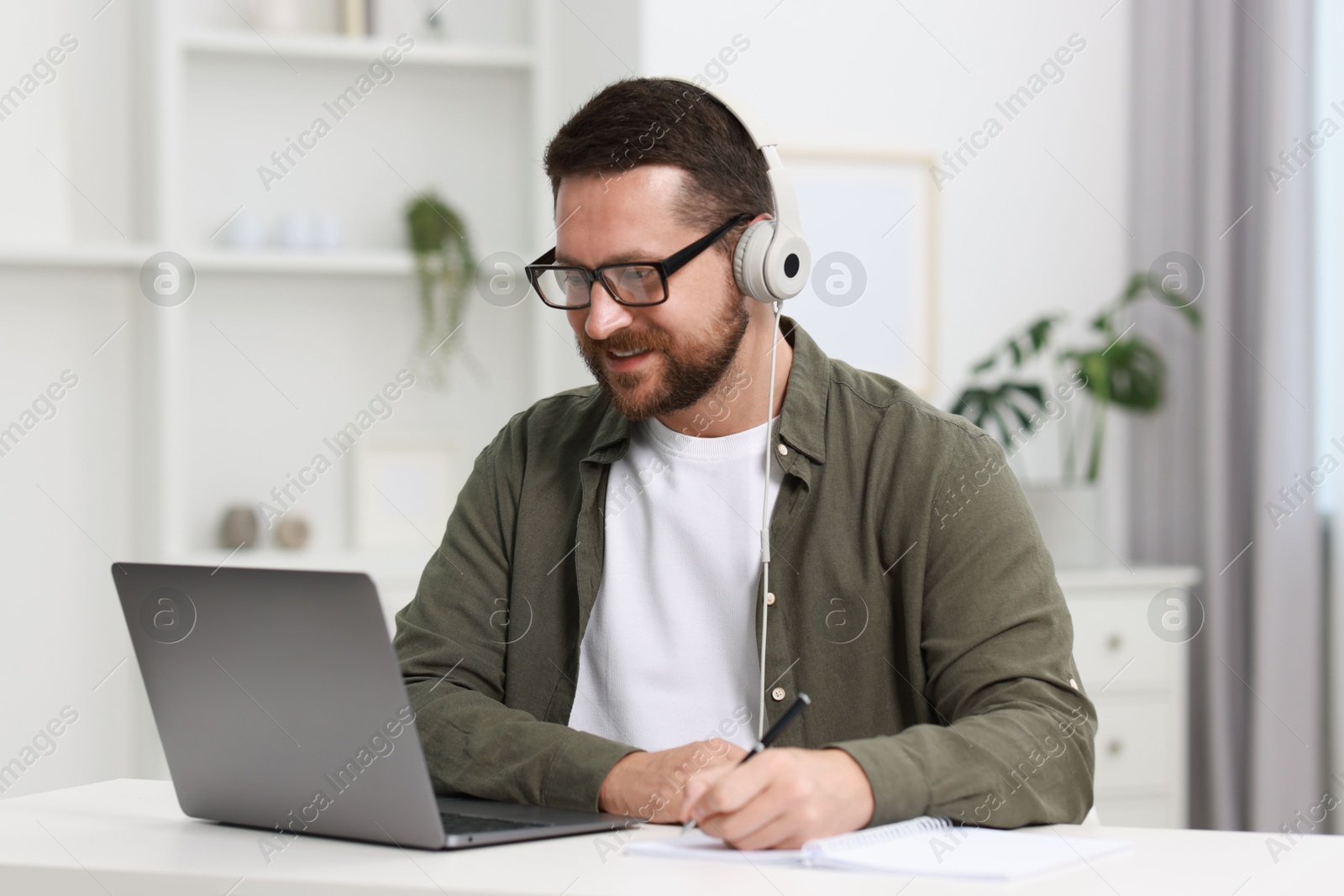 Photo of Interpreter in headphones having video chat via laptop at white table indoors