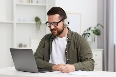 Interpreter in headphones having video chat via laptop at white table indoors