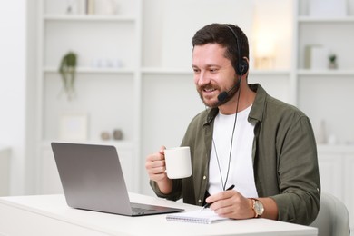 Interpreter in headset having video chat via laptop at white table indoors