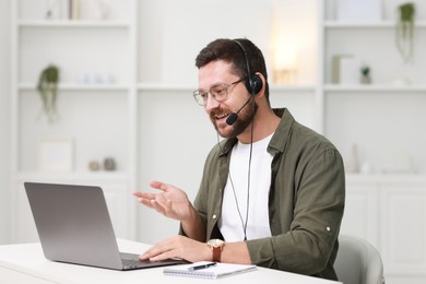 Interpreter in headset having video chat via laptop at white table indoors