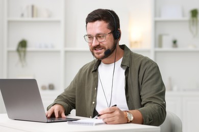 Interpreter in headset having video chat via laptop at white table indoors