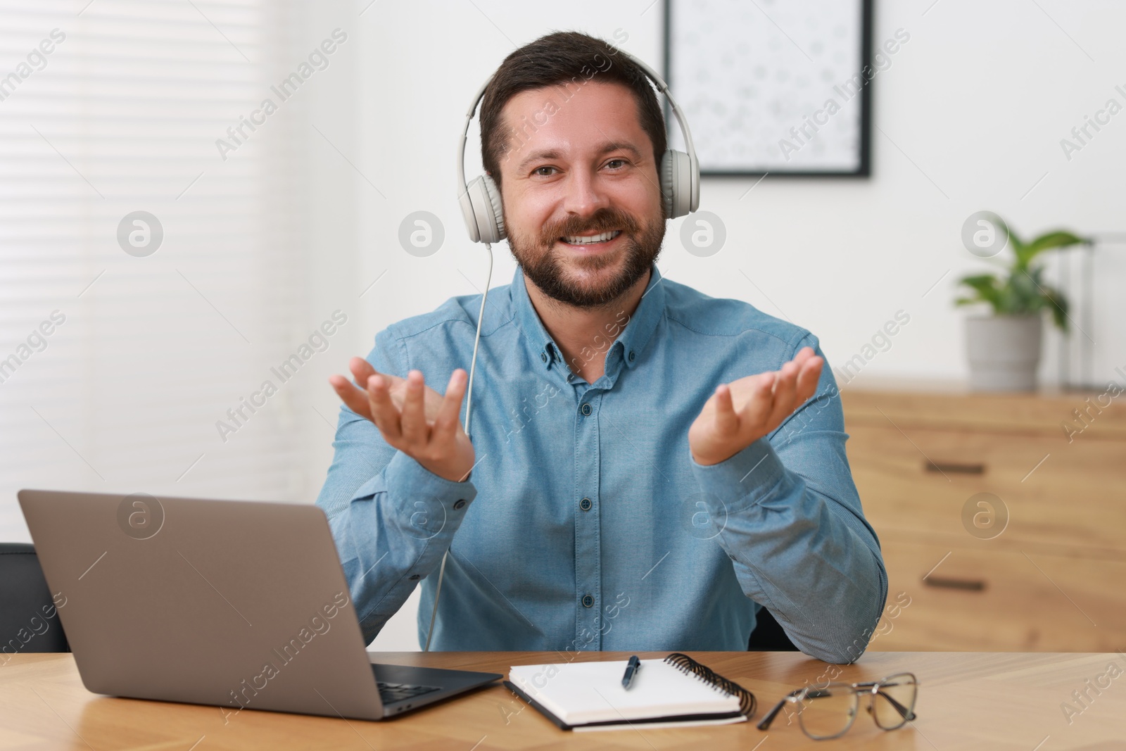 Photo of Interpreter in headphones having video chat via laptop at wooden table indoors