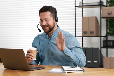 Interpreter in headset having video chat via laptop at wooden table indoors