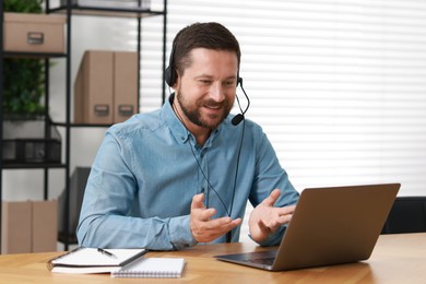 Interpreter in headset having video chat via laptop at wooden table indoors