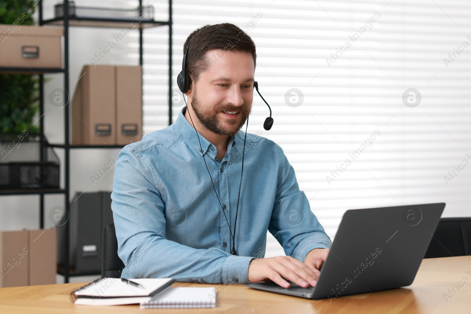 Photo of Interpreter in headset having video chat via laptop at wooden table indoors