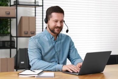 Photo of Interpreter in headset having video chat via laptop at wooden table indoors