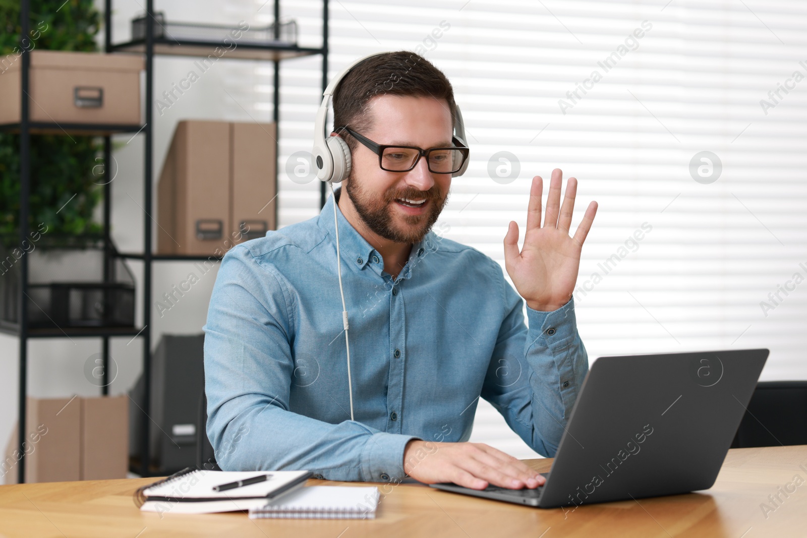 Photo of Interpreter in headphones having video chat via laptop at wooden table indoors