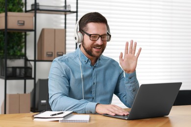 Photo of Interpreter in headphones having video chat via laptop at wooden table indoors