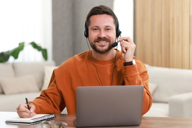 Interpreter in headset having video chat via laptop at wooden table indoors