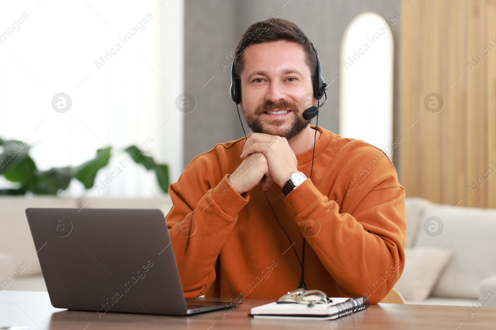 Photo of Interpreter in headset having video chat via laptop at wooden table indoors