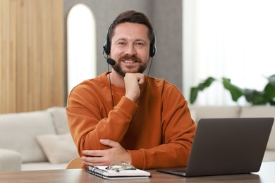 Interpreter in headset having video chat via laptop at wooden table indoors