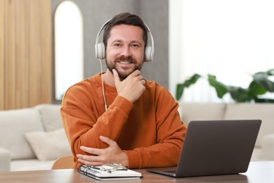 Photo of Interpreter in headphones having video chat via laptop at wooden table indoors