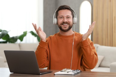 Interpreter in headphones having video chat via laptop at wooden table indoors