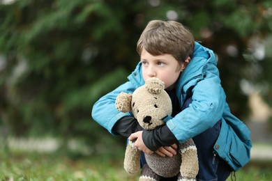 Autism concept. Lonely little boy with teddy bear outdoors, space for text