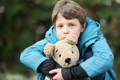 Photo of Autism concept. Lonely little boy with teddy bear outdoors