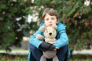 Autism concept. Lonely little boy with teddy bear outdoors