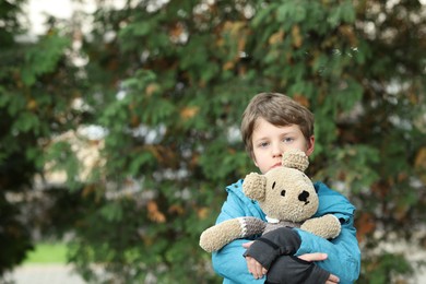 Autism concept. Lonely little boy with teddy bear outdoors, space for text