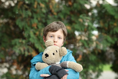 Autism concept. Lonely little boy with teddy bear outdoors